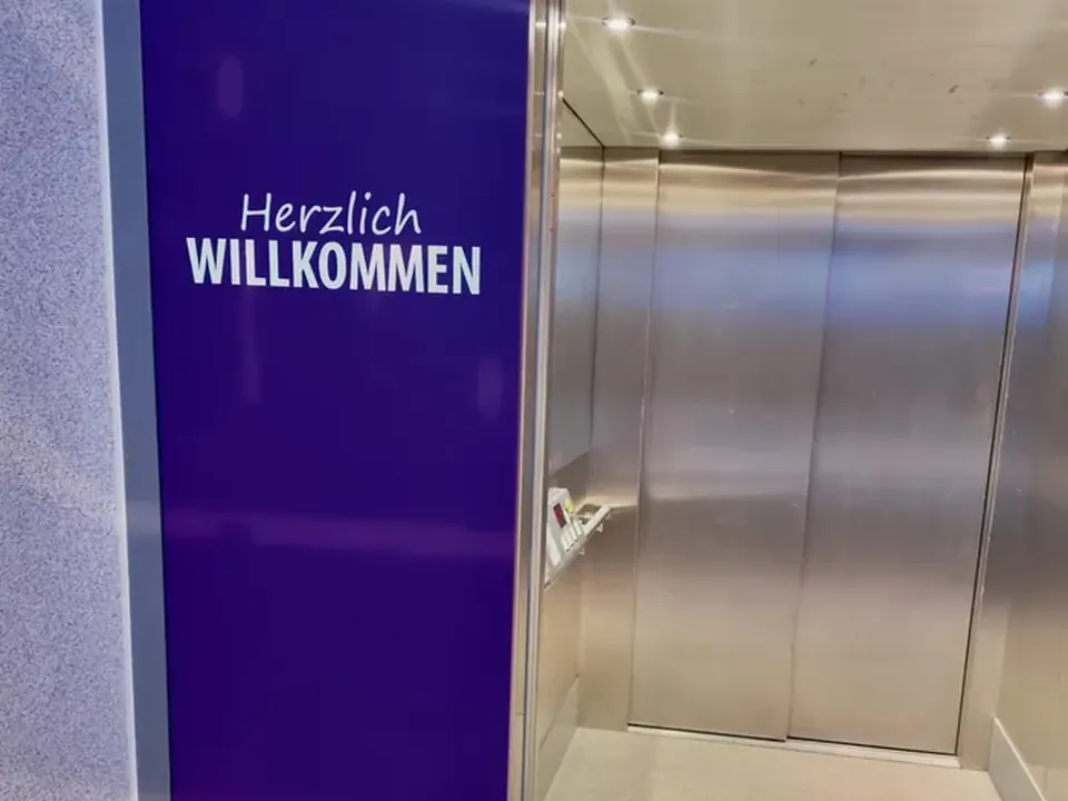 Aufzug mit lila Wand und Schriftzug Herzlich willkommen